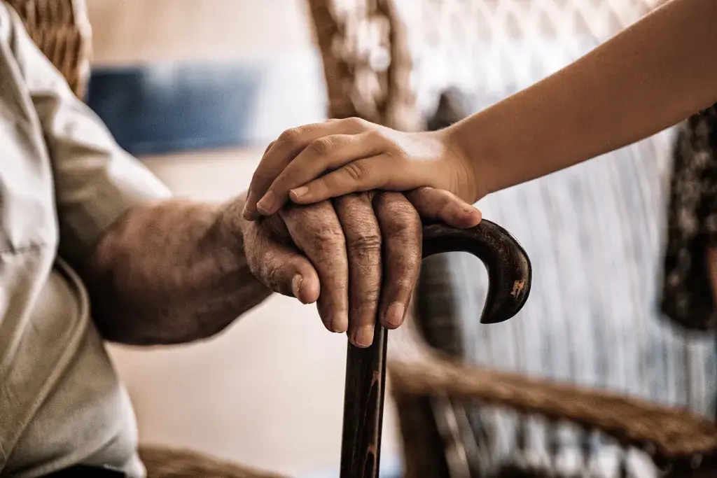 Childs hand over older adult mans hand holding a cane.