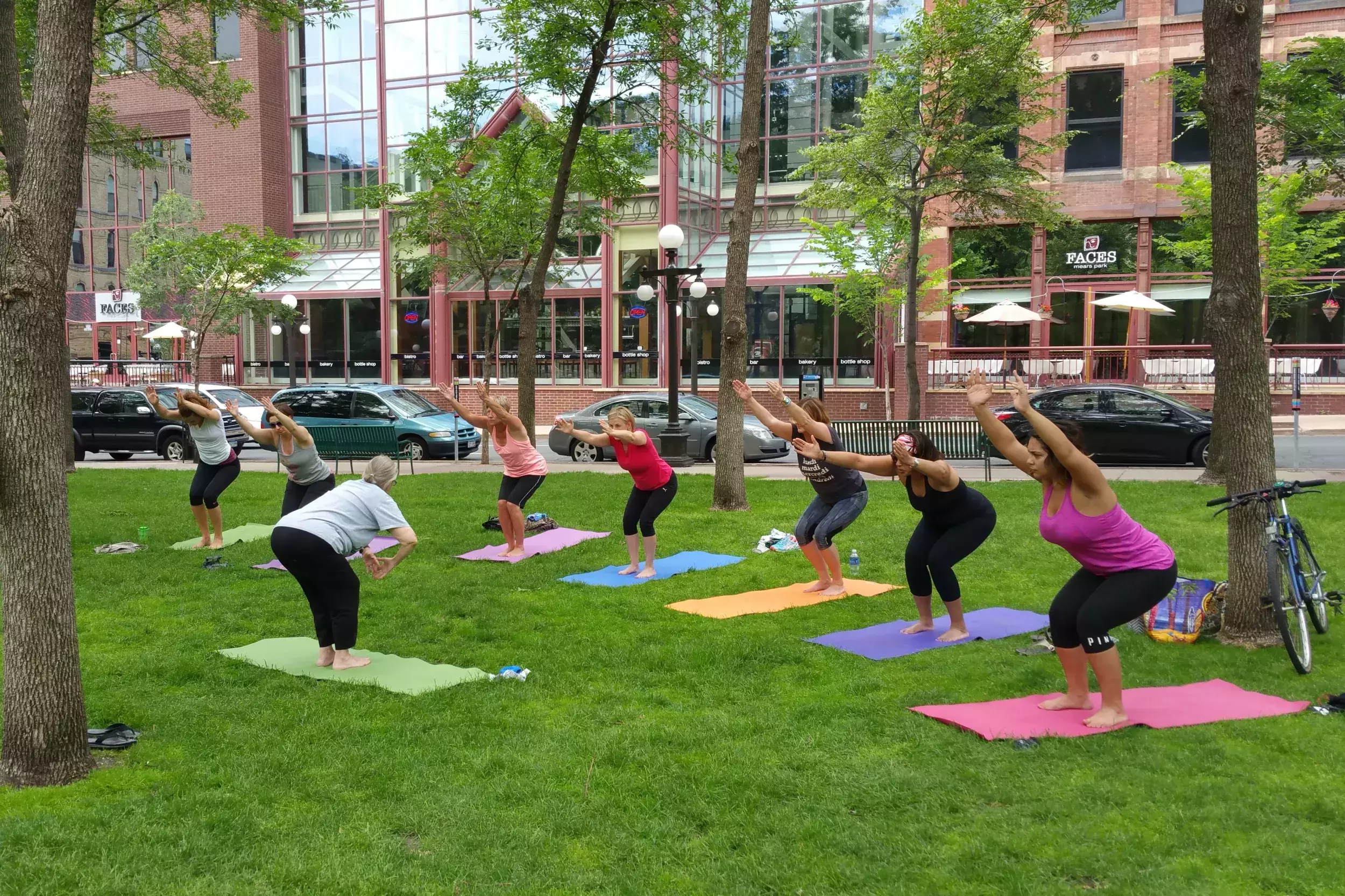 A group of people stretching on yoga mats on the grass at Mears Park during a Fitness in the Parks class.