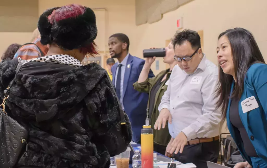 People are standing around a table having a conversation in a school gym.