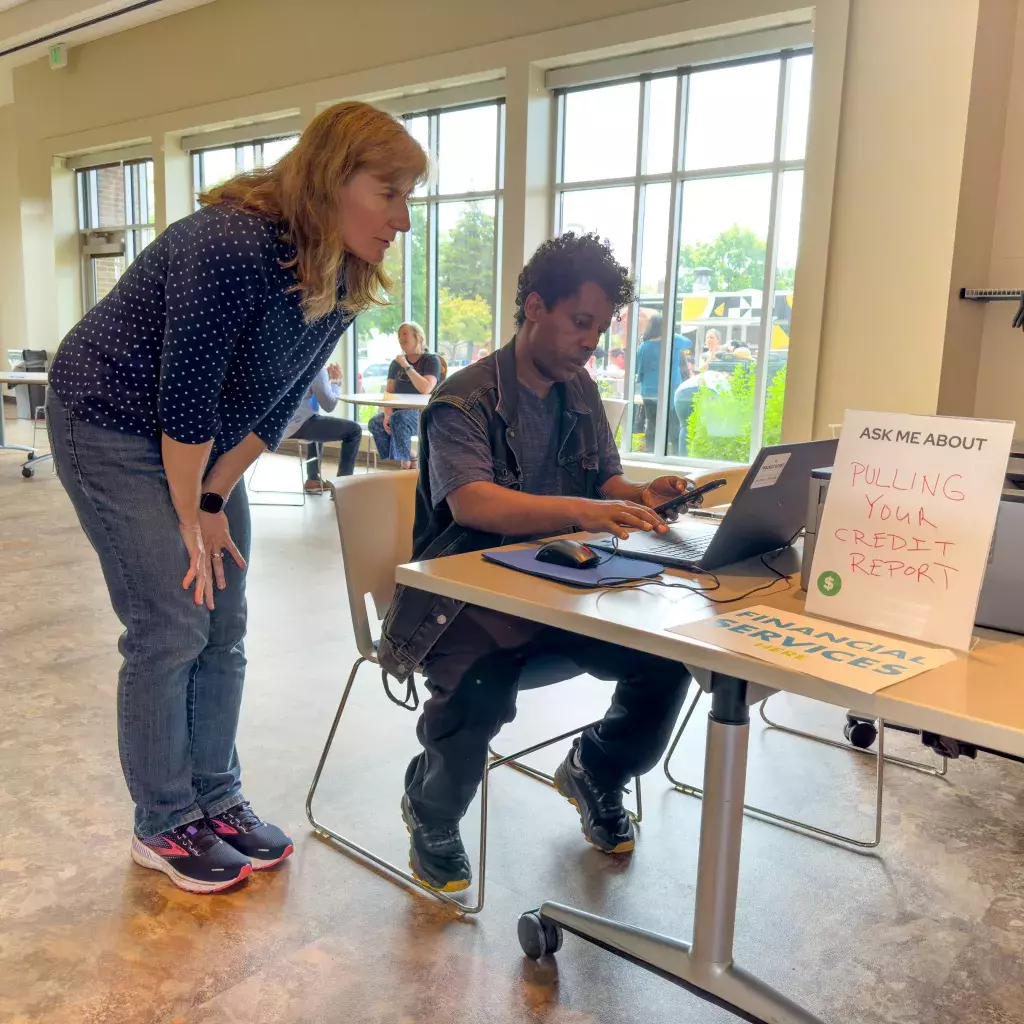 Man sitting at computer and women assisting him. 