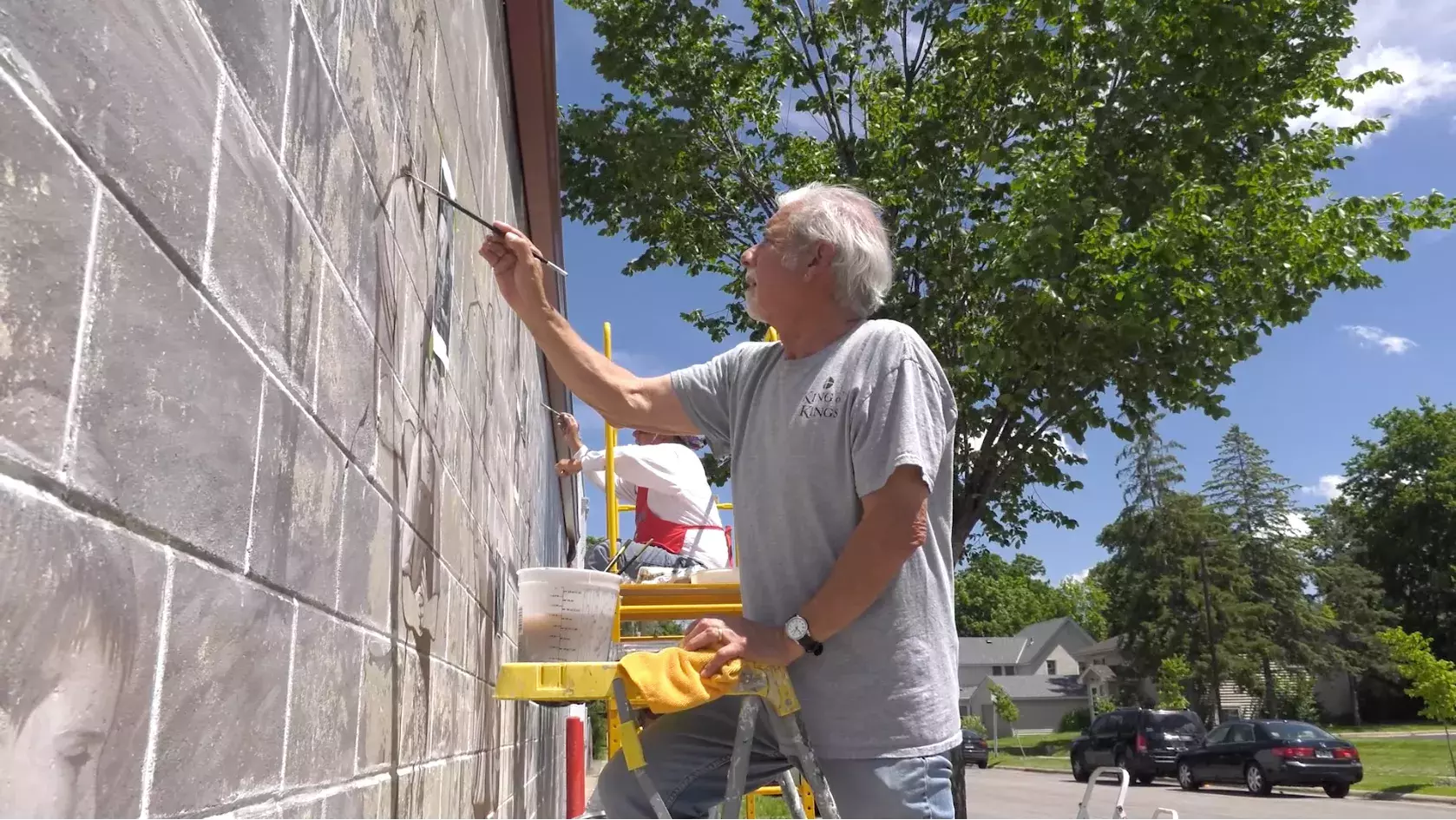 Man painting large mural on the side of Captain Ken's Foods.