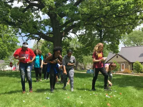 Teens collect ping-pong balls scattered in the grass