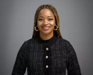 Portrait of Ward 1 Councilmember Anika Bowie smiling in a black suit in front of a gray background. Photo credit: Rich Ryan.