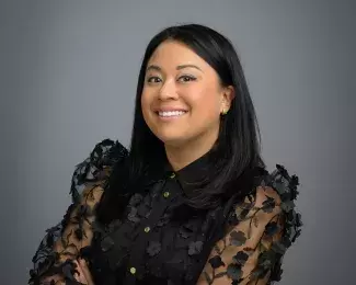 Photo of Ward 4 Council President Mitra Jalali smiling in a black blouse in front of a gray background. Photo credit: Rich Ryan.