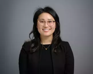 Photo of Ward 5 Council Vice President HwaJeong Kim smiling in a black suit in front of a gray background. Photo credit: Rich Ryan.